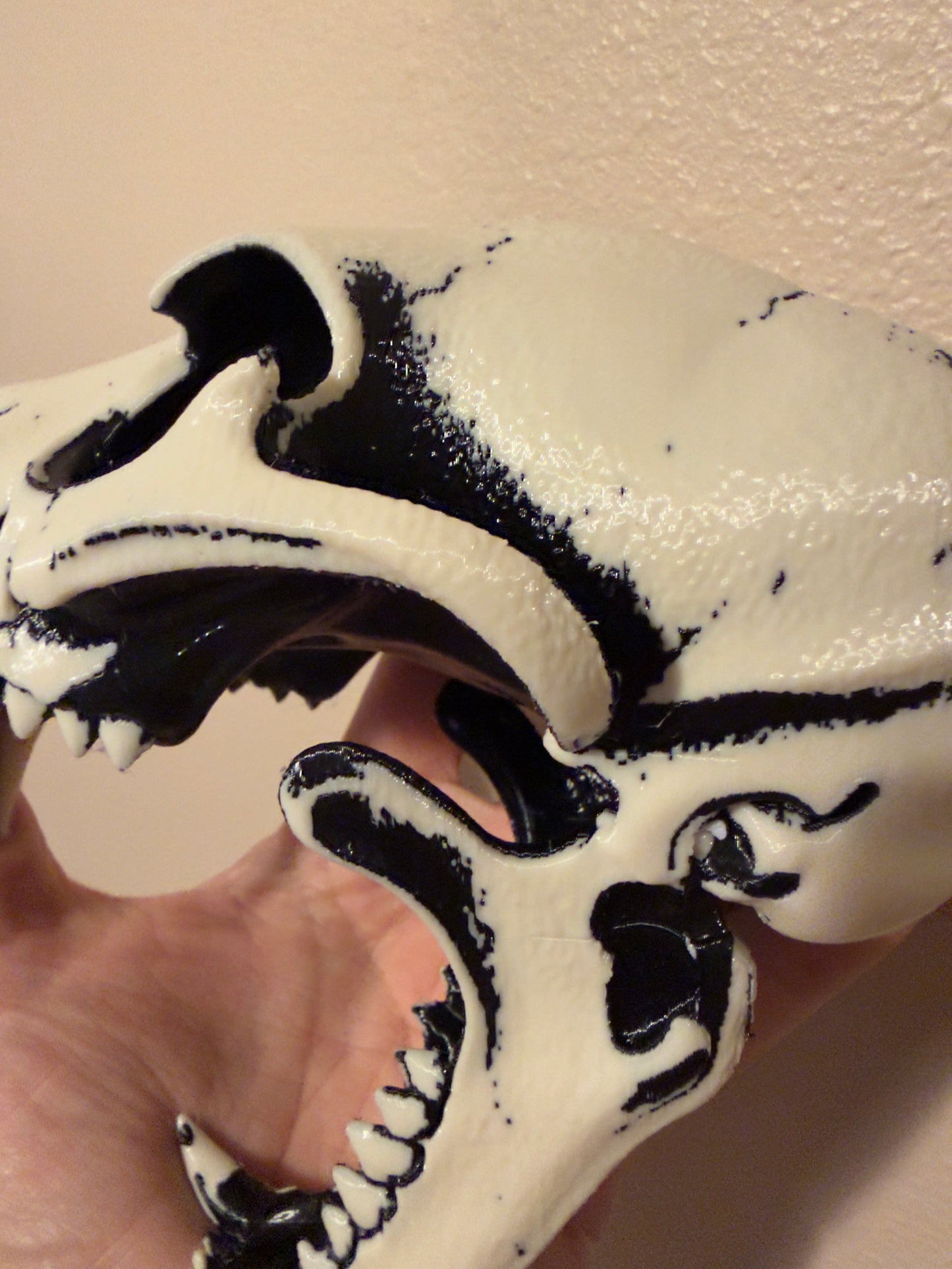 A close-up of a white and black marbled skull-shaped object being held by a hand against a beige wall.