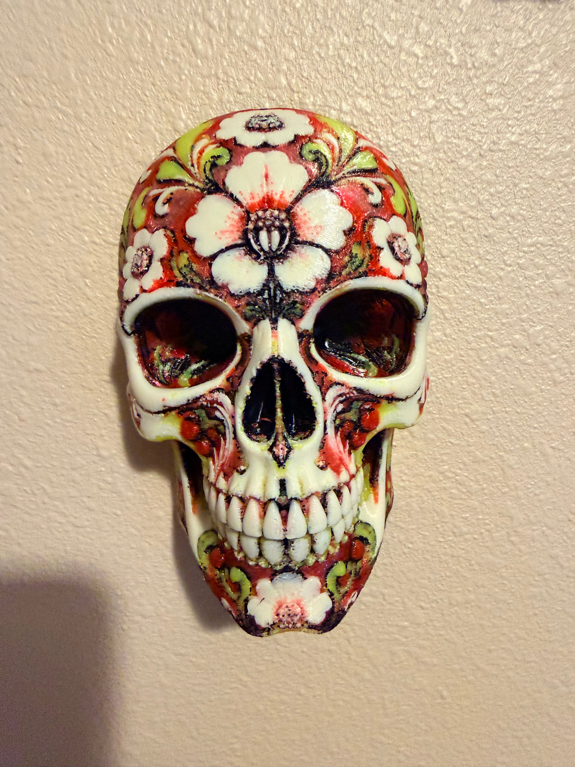 A decorative skull with a colorful floral and paisley pattern, mounted on a textured beige wall.