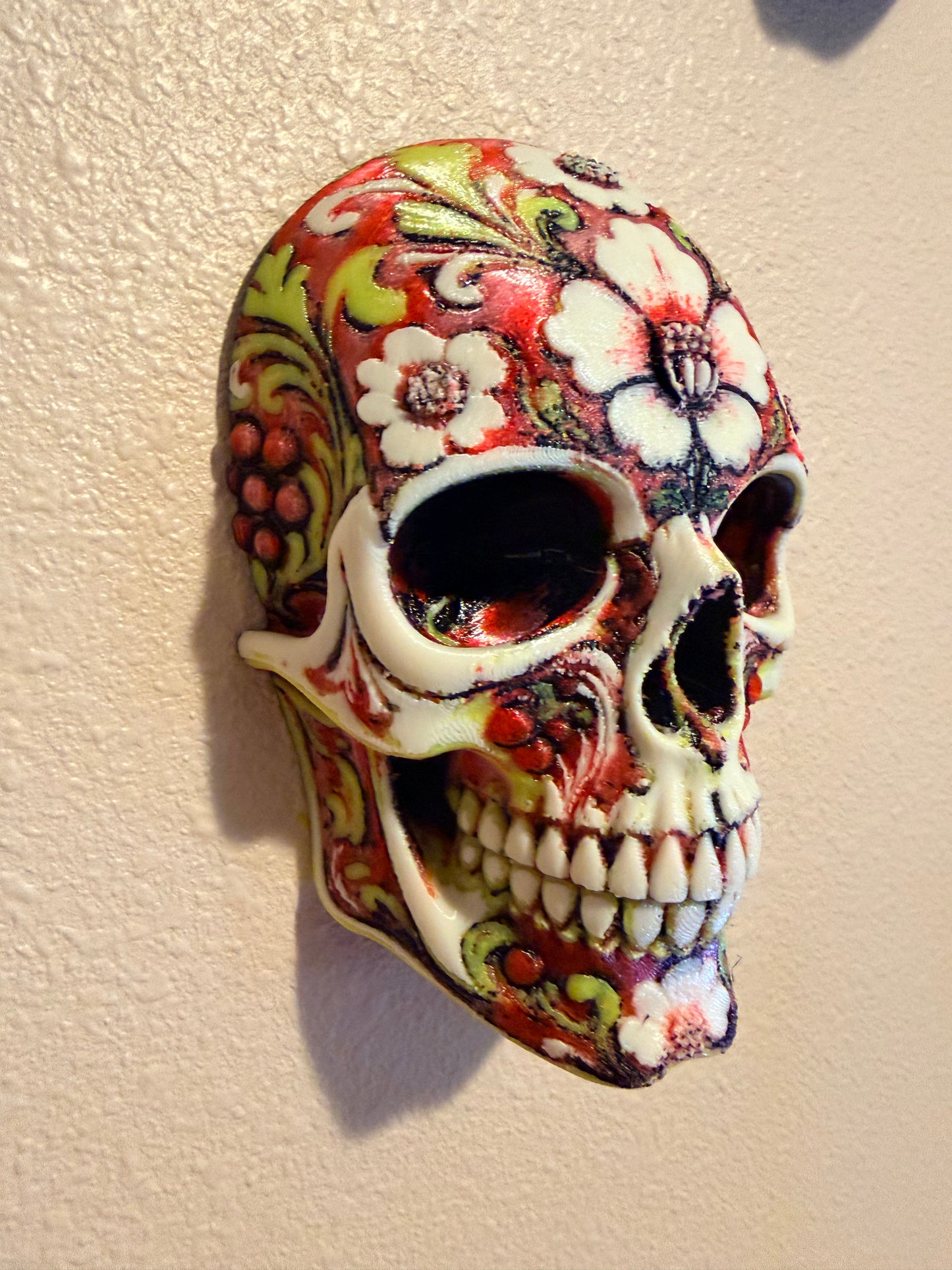 A decorative ceramic skull with a colorful floral and scroll pattern, photographed on a textured beige surface.